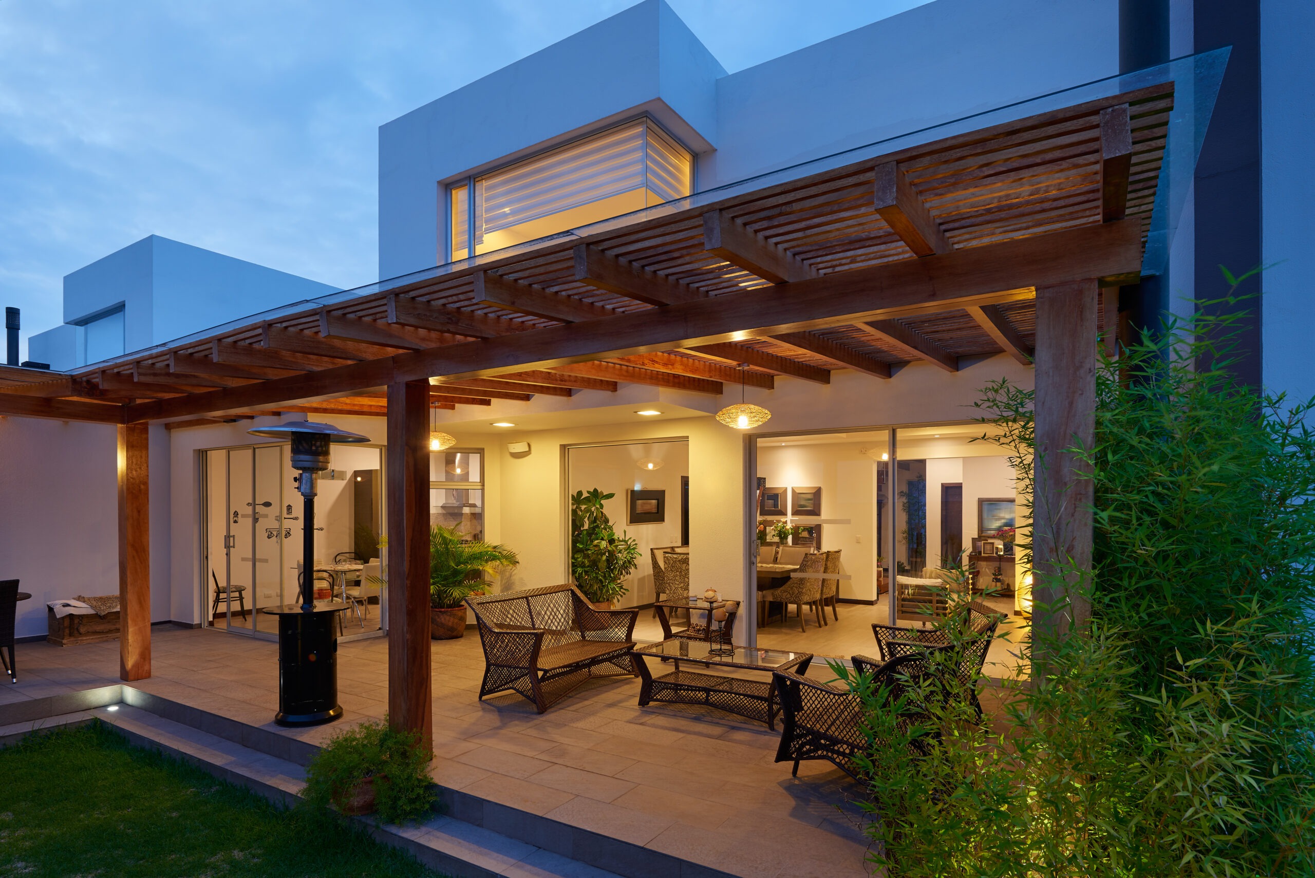 Modern outdoor patio with comfortable seating and a heater, illuminated at dusk, showcasing a relaxing space adjacent to a stylish indoor area.