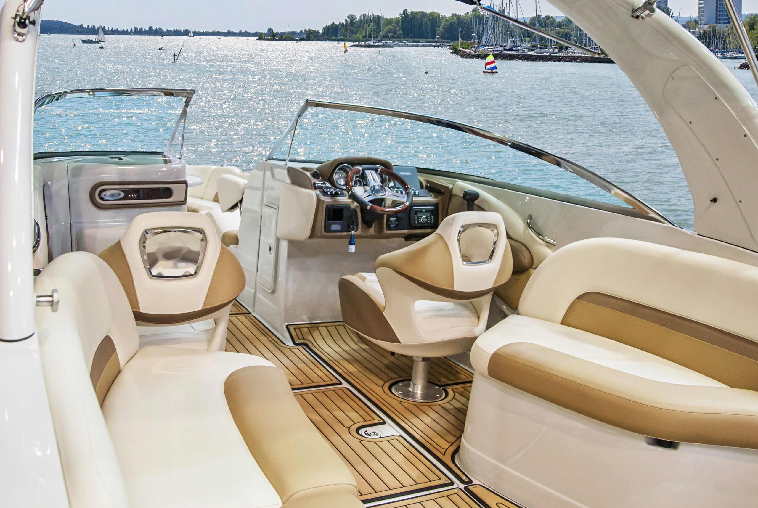 Modern boat interior featuring beige and white seating, a steering console, and scenic water views, ideal for leisure or navigation.